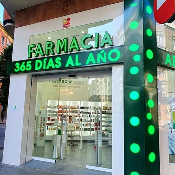 Façade of Farmacia Vegas with the lit green cross — open every day